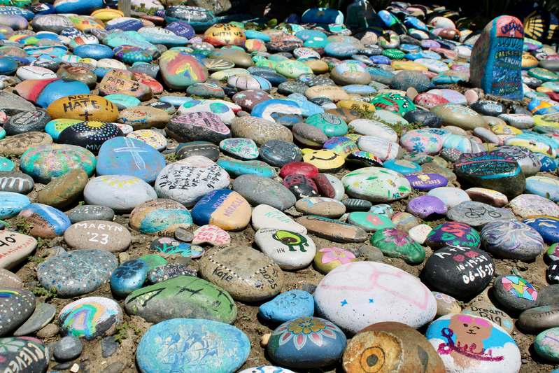 A curated flat-lay of painted rocks, watercolor brushes, natural stones, and open sketchbook on wooden table